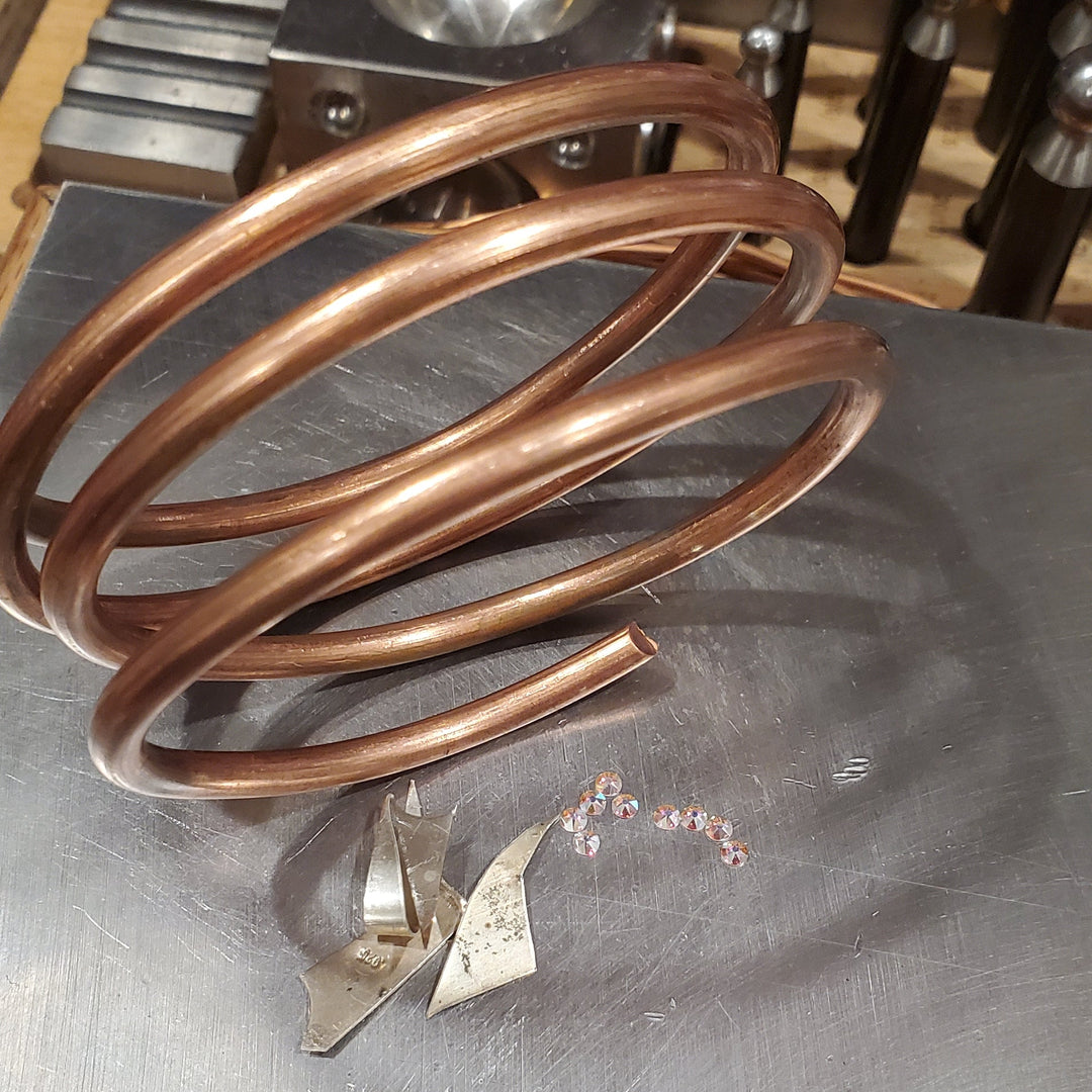 picture of 4 gauge raw solid copper coil besides sterling silver scrap pieces and flat swarovki crystals placed on stainless steel anvil.