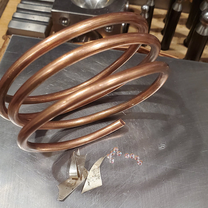 picture of 4 gauge raw solid copper coil besides sterling silver scrap pieces and flat swarovki crystals placed on stainless steel anvil.