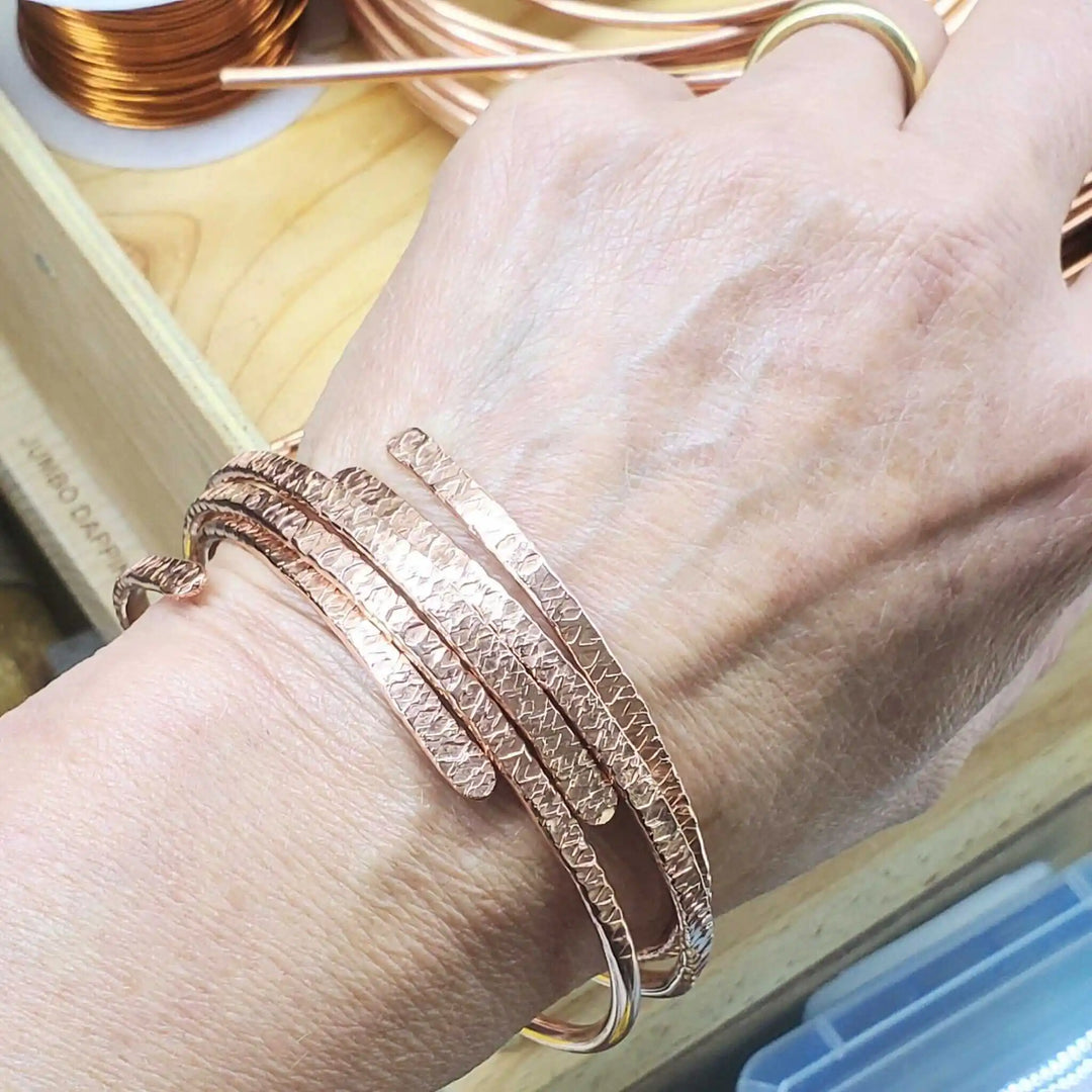 Unisex 8 Gauge Adjustable Hammered Copper Overlap Bangle worn on a hand with multiple copper bracelets.