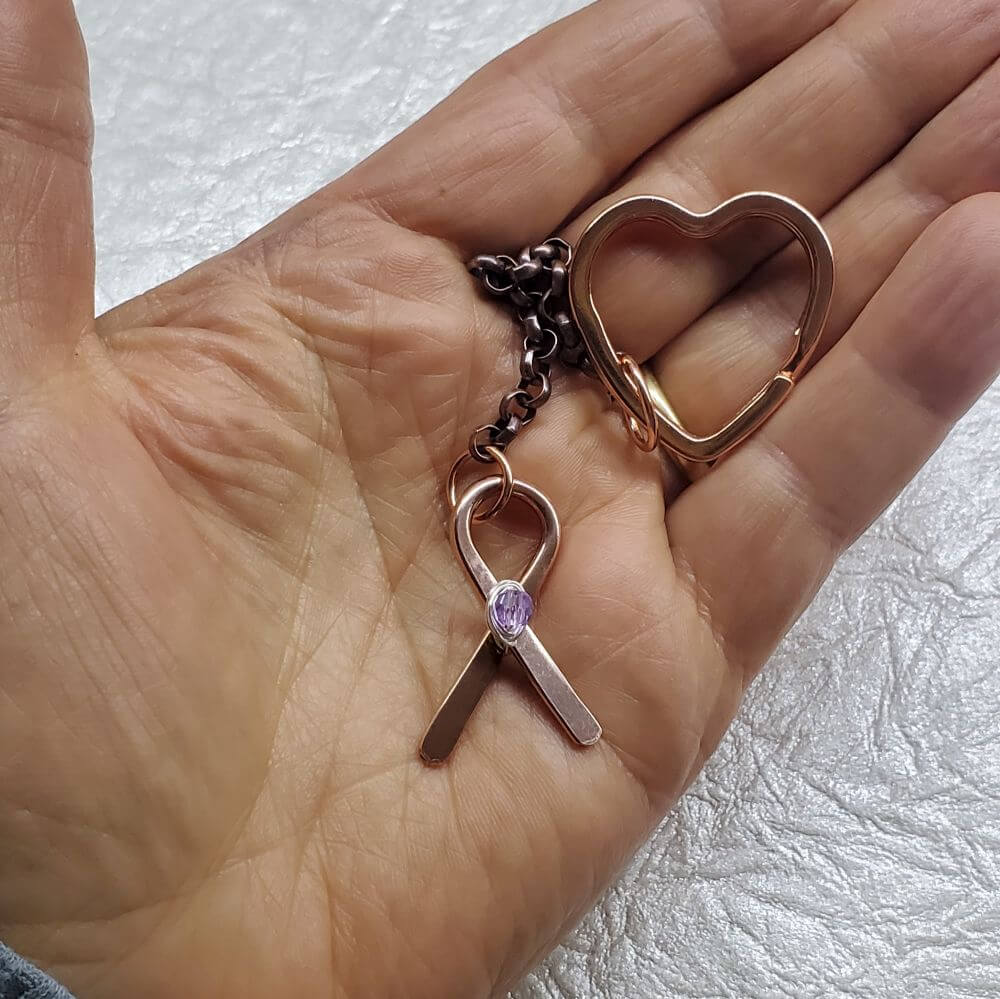 Rose gold heart-shaped keychain with a pink ribbon charm on a hand against a light background