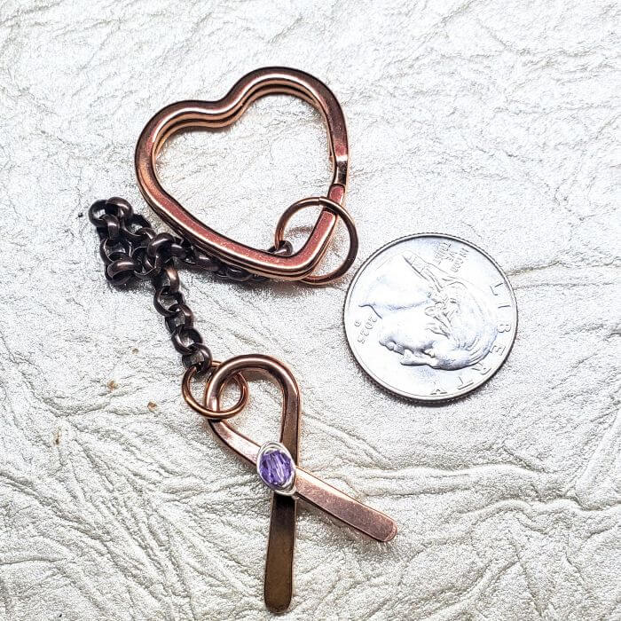 Copper keychain with heart-shaped keyring and purple gemstone on a textured surface.