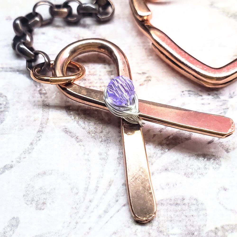 Rose gold cross keychain with purple gemstone on a textured surface