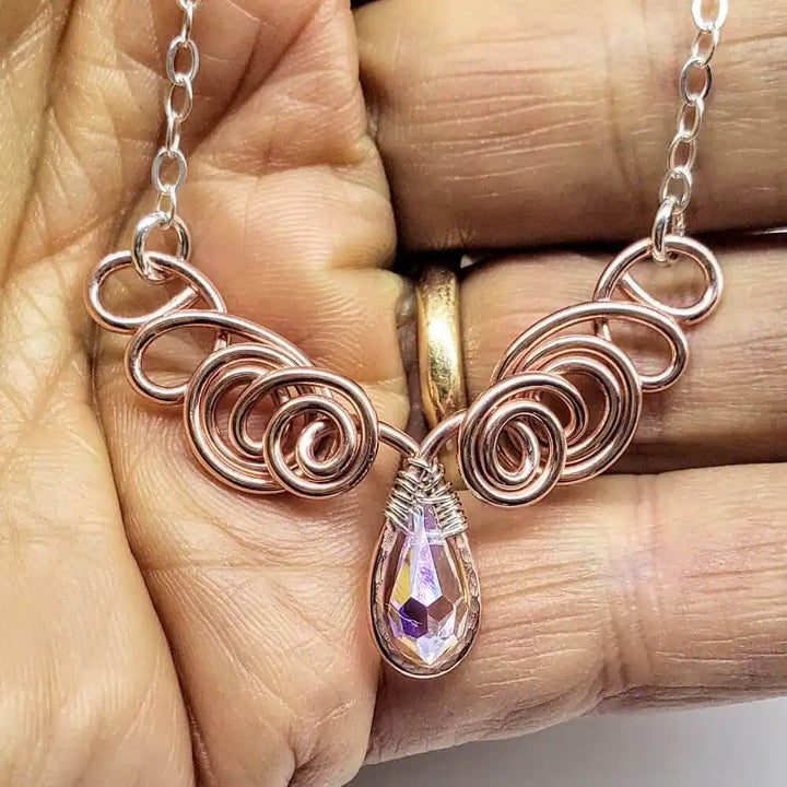 Handmade Sculpted Copper Silver Angel in Flight Necklace displayed in a hand, showcasing intricate design and sparkling drop pendant.