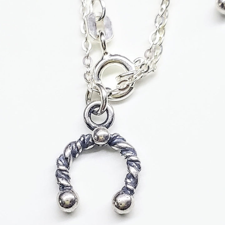 Close-up of handmade sterling silver horseshoe jewelry pendant on a chain.