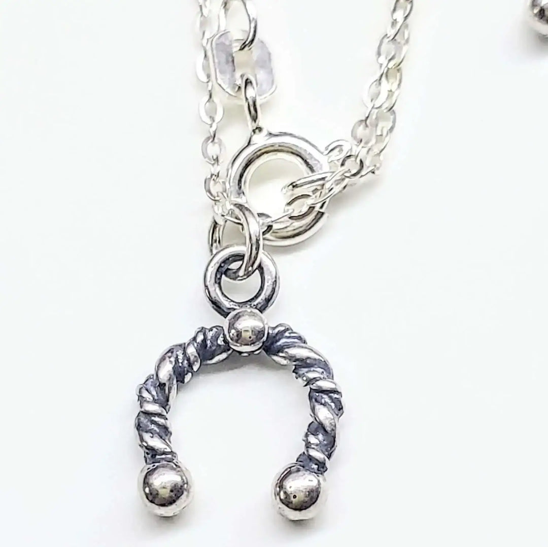 Handmade sterling silver horseshoe jewelry pendant on a chain, showcasing artisan craftsmanship and charm.