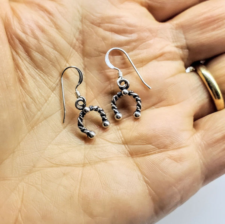 Handmade sterling silver horseshoe jewelry earrings displayed in a hand, showcasing artisan craftsmanship and lucky charm.
