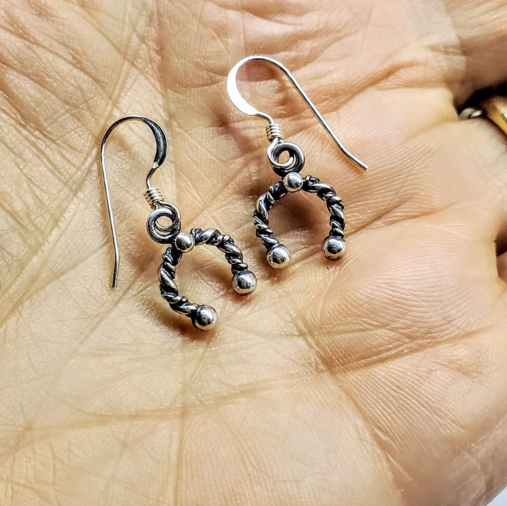 Handmade sterling silver horseshoe jewelry earrings displayed on a hand, showcasing intricate design and craftsmanship.