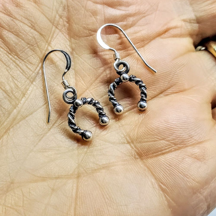 Handmade sterling silver horseshoe jewelry earrings displayed on a hand, showcasing intricate design and craftsmanship.