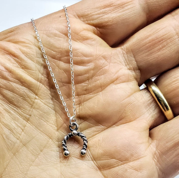 Handmade sterling silver horseshoe jewelry pendant on a chain, showcasing artisan craftsmanship and lucky charm style.