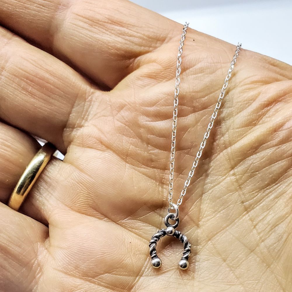 Handmade sterling silver horseshoe jewelry pendant on a delicate chain held in a hand, showcasing artisan craftsmanship.