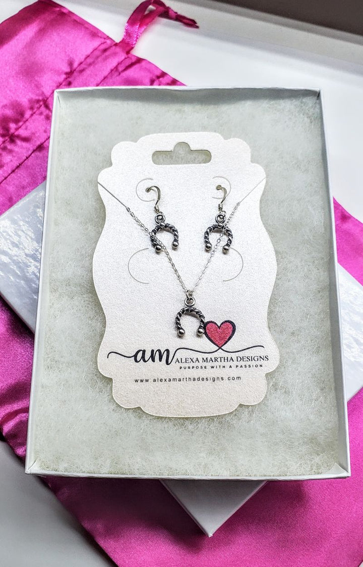 Handmade sterling silver horseshoe jewelry set displayed in a box with pink fabric background.
