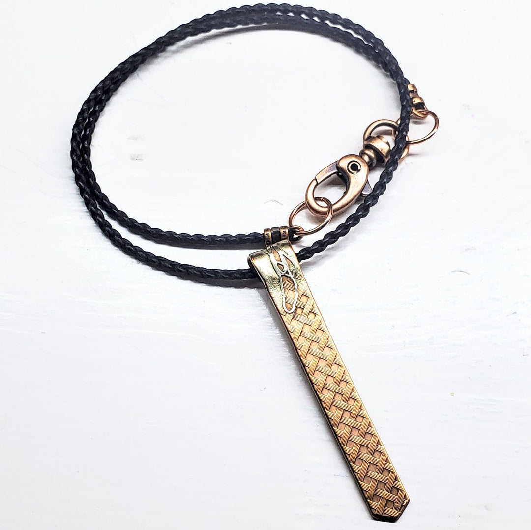 Necklace with a braided black cord and woven wooden pendant on a white background