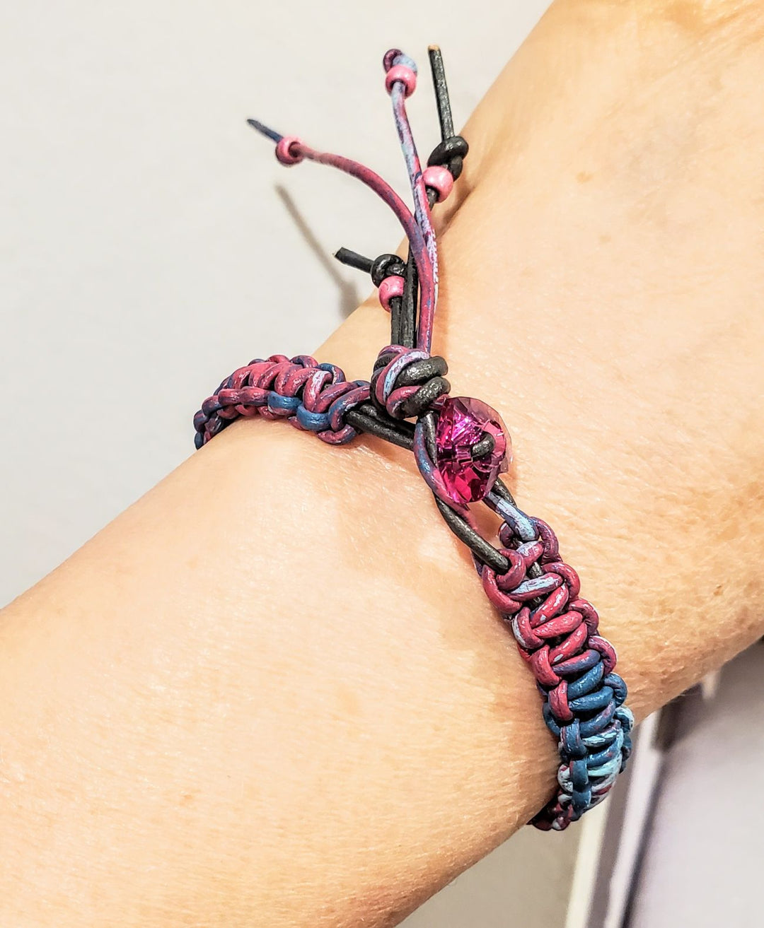 Macrame tie-dye leather Crystal bracelet showcased on a wrist, featuring vibrant pink, blue, and black colors with a sparkling crystal.
