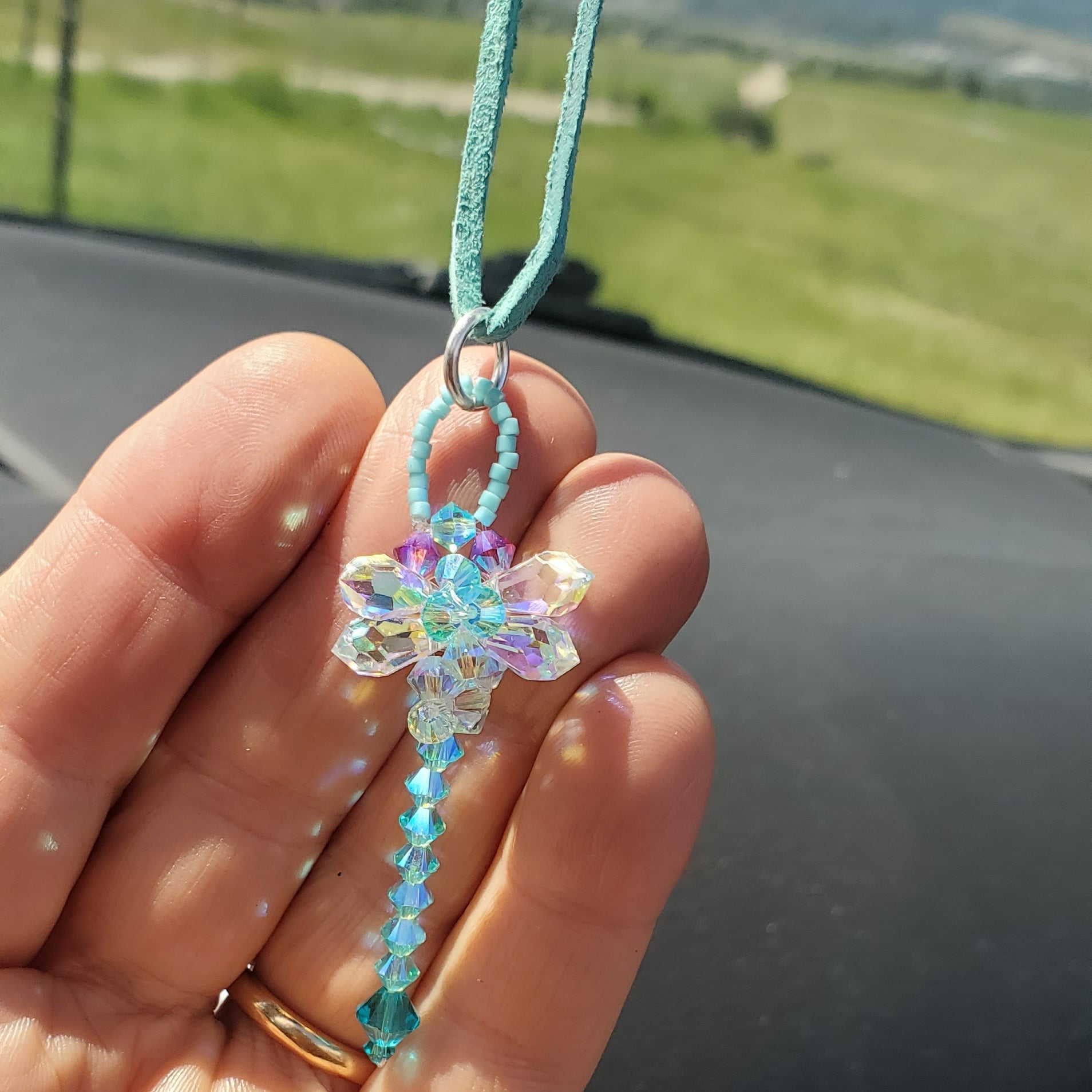 Beaded 3-D Rearview Mirror Colored Crystal Dragonfly Charm hanging from a hand in a car, showcasing teal and aquamarine crystals.
