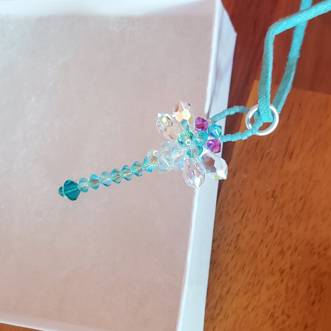 Beaded 3-D Rearview Mirror Colored Crystal Dragonfly Charm hanging from a string on a wooden surface.