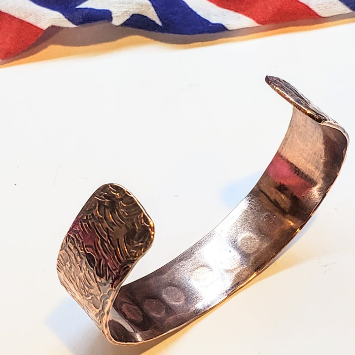 Antiqued copper cuff with textured design on a white background