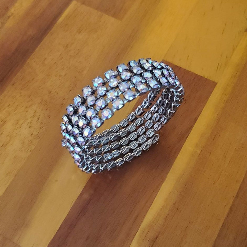 A silver-toned multi-band bracelet with rows of clear stones, photographed on a wooden tabletop.