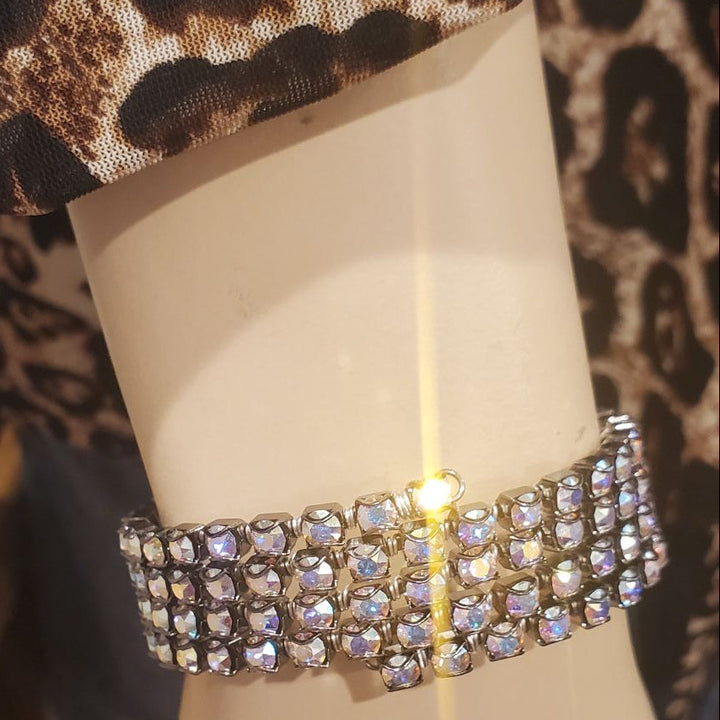 A wide, multi-row rhinestone bracelet displayed on a beige mannequin wrist, with a leopard-print fabric visible above it.