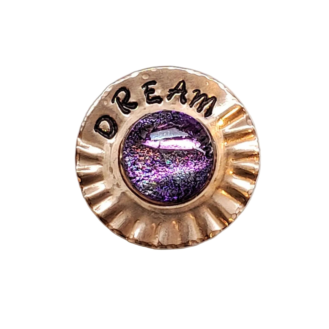A round, scalloped rose gold button or pin featuring the word &