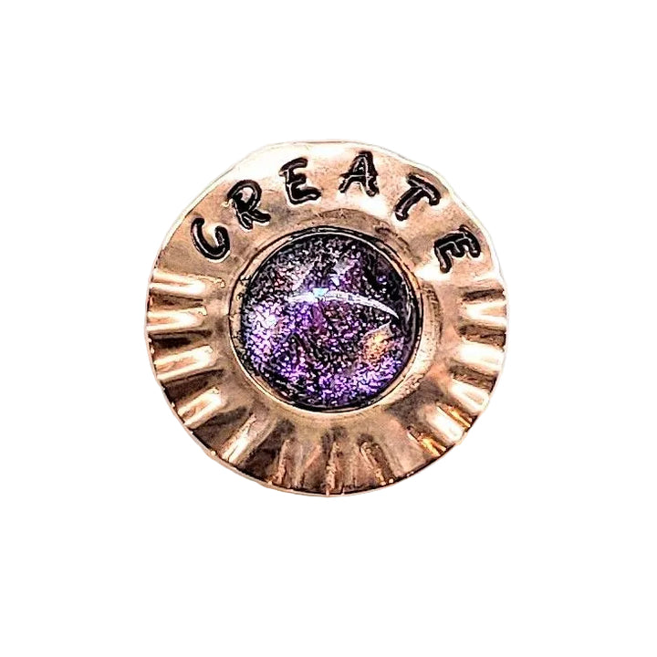 A round, scalloped copper-toned metal button or pin featuring the word &
