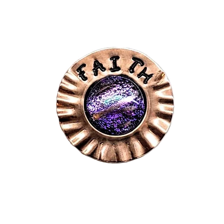 A circular bronze-toned metal pin or brooch with a scalloped edge, the word &