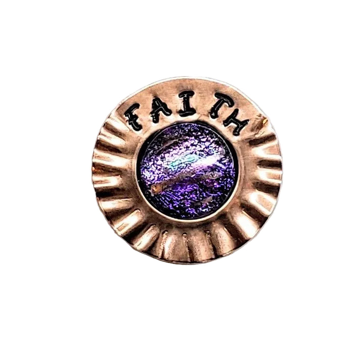 A circular bronze-toned metal pin or brooch with a scalloped edge, the word &