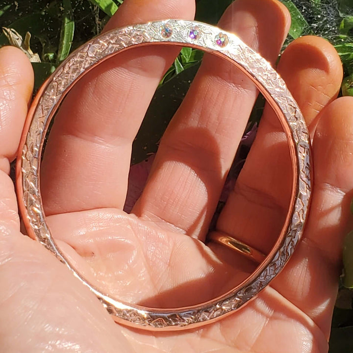 A rose gold bangle bracelet with small clear stones set along the outer edge, held in a person&