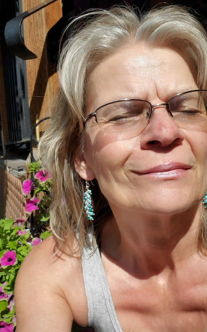 Woman wearing Seen On Jane The Virgin Silver Turquoise Wire Coil Earrings, smiling in sunlight with flowers in the background.