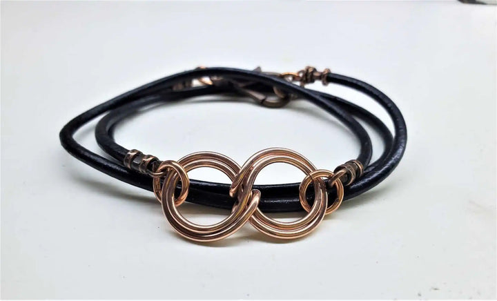 Copper Double Infinity Gender Neutral Leather Wrap Bracelet on a white background with black leather cord and intertwined copper symbols.