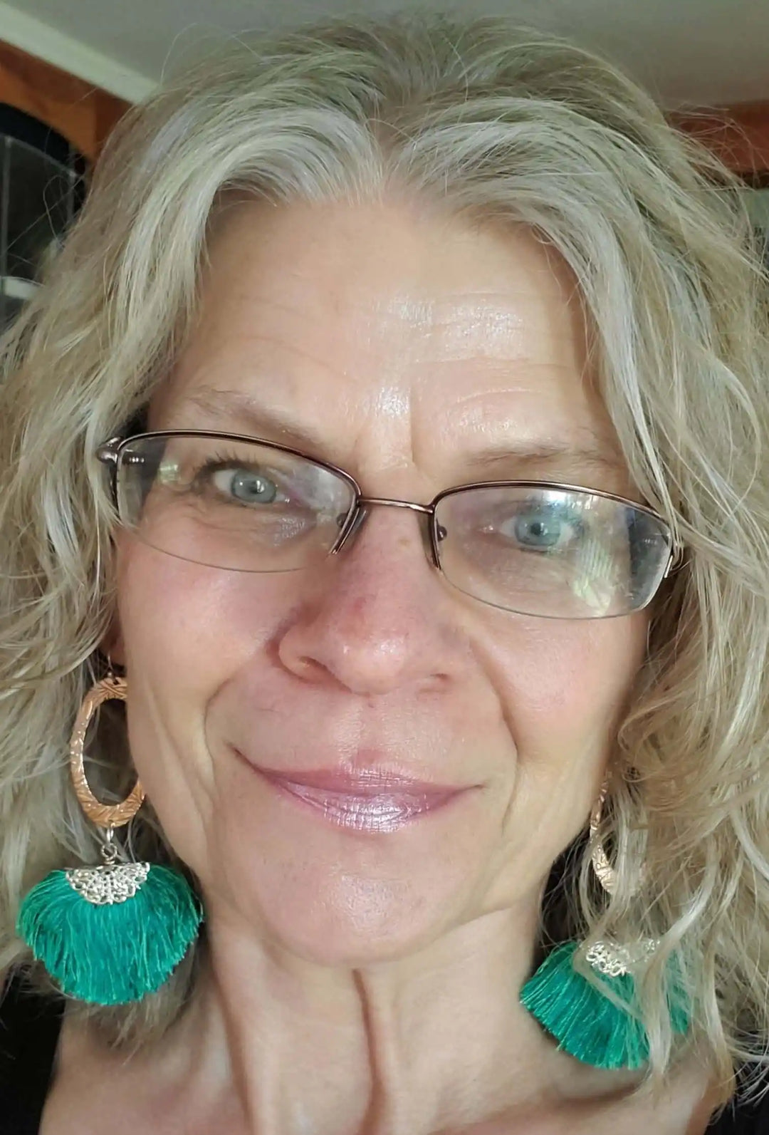 Rose Gold Filigree Silk Tassel Earrings Copper Embossed worn by a woman with curly hair and glasses, showcasing green tassels.
