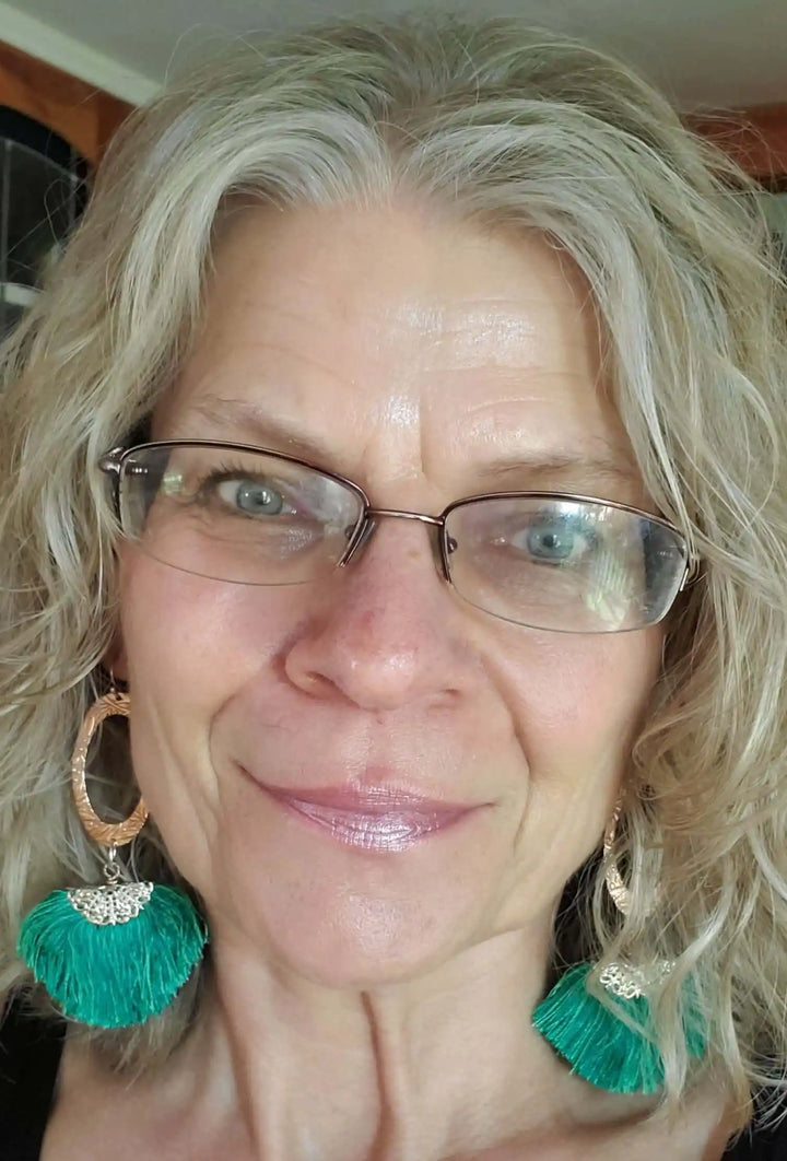 Rose Gold Filigree Silk Tassel Earrings Copper Embossed worn by a woman with curly hair and glasses, showcasing green tassels.