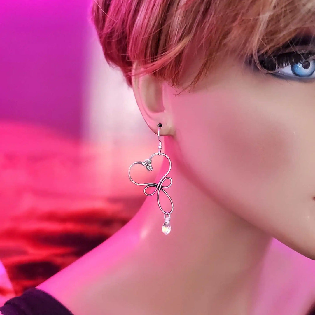 Handmade Copper Wire Sculpted Heart Crystal Drop Earrings displayed on a mannequin with a pink background.
