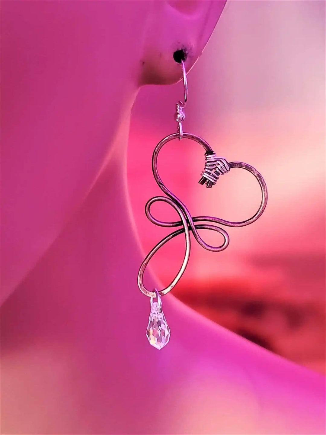 Handmade Copper Wire Sculpted Heart Crystal Drop Earrings displayed on a mannequin against a vibrant pink background.