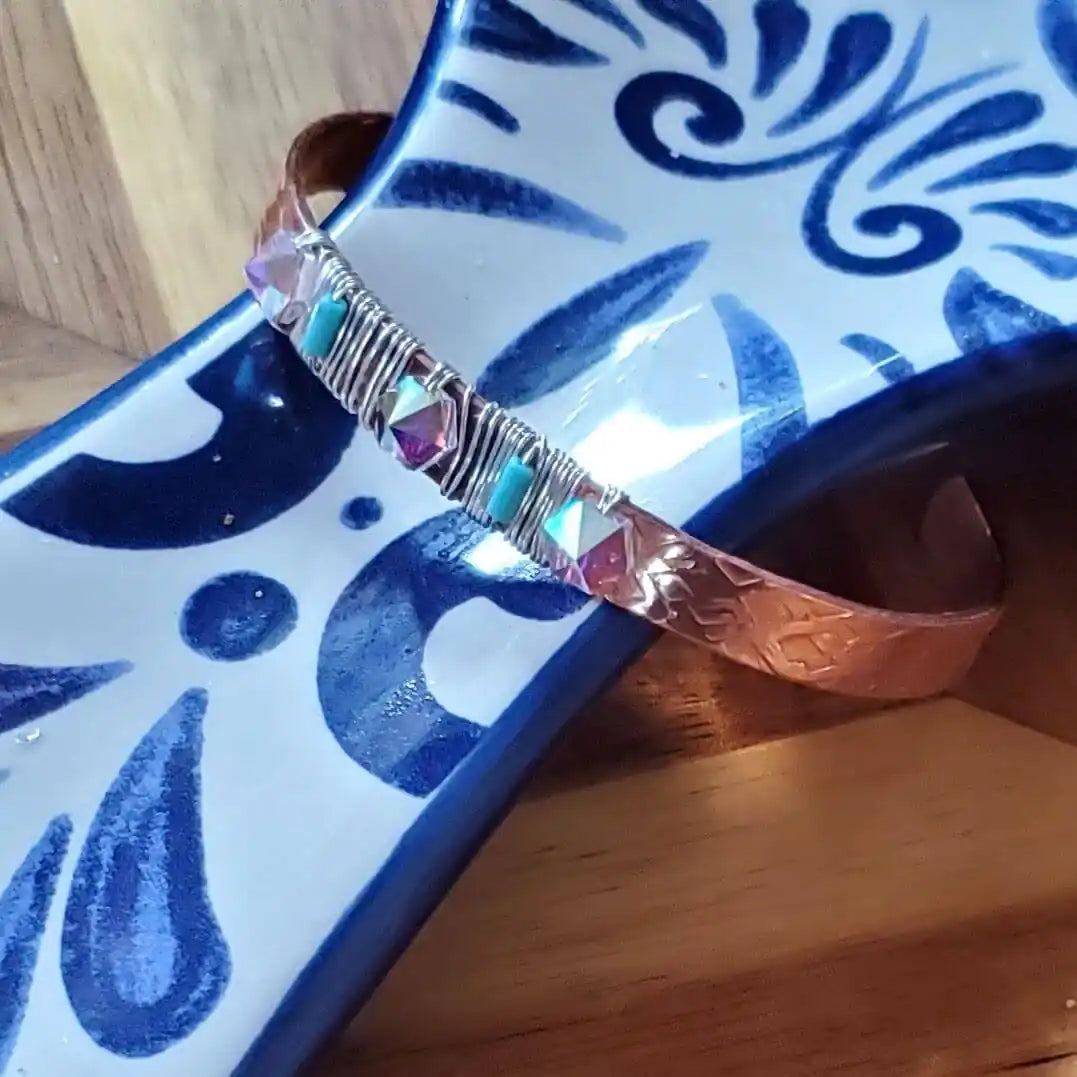 Handmade Copper Turquoise Crystal Spike Cuff on decorative plate, showcasing its edgy artisan design and colorful accents.