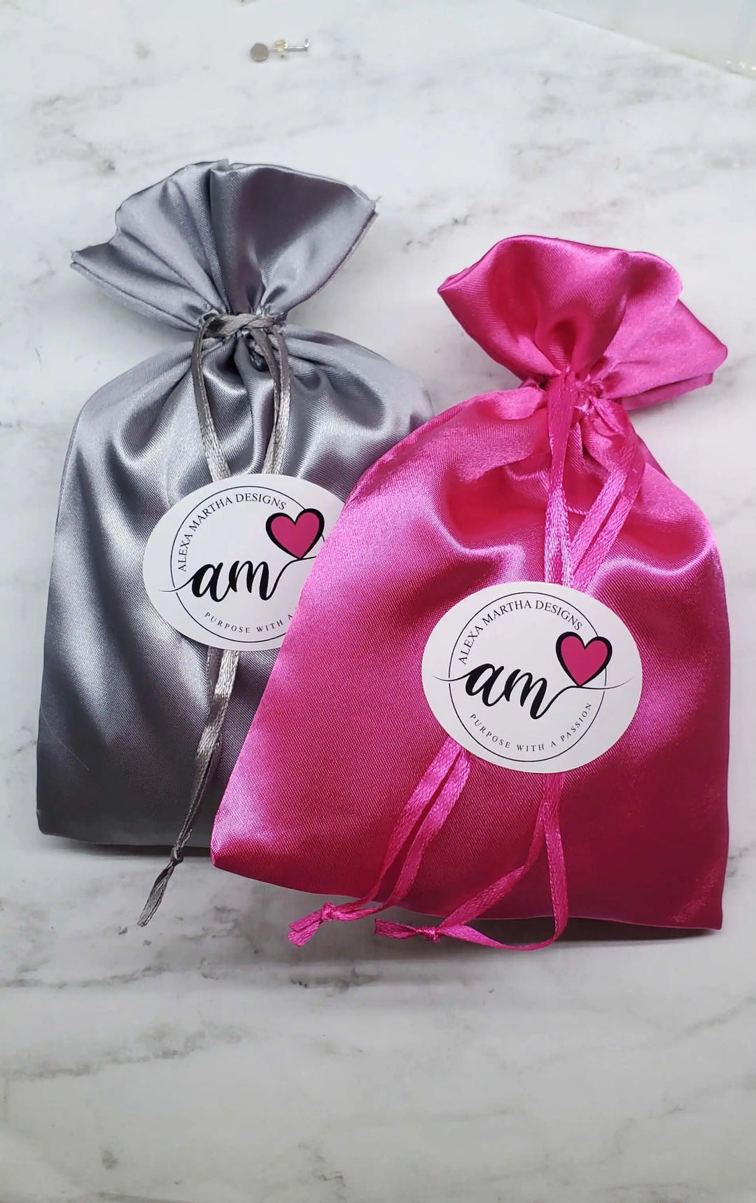 Two satin gift bags in gray and pink with labels, showcasing elegant packaging for jewelry or accessories.