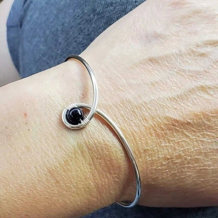 Silver Blue Bead Child Abuse Awareness Ribbon Bangle worn on a wrist, featuring a silver bangle with a blue sandstone bead.
