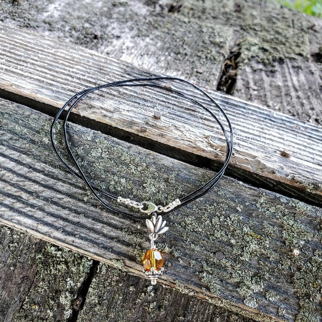 Handmade silver crystal pineapple leather necklace with yellow Austrian Swarovski crystal on a wooden background.