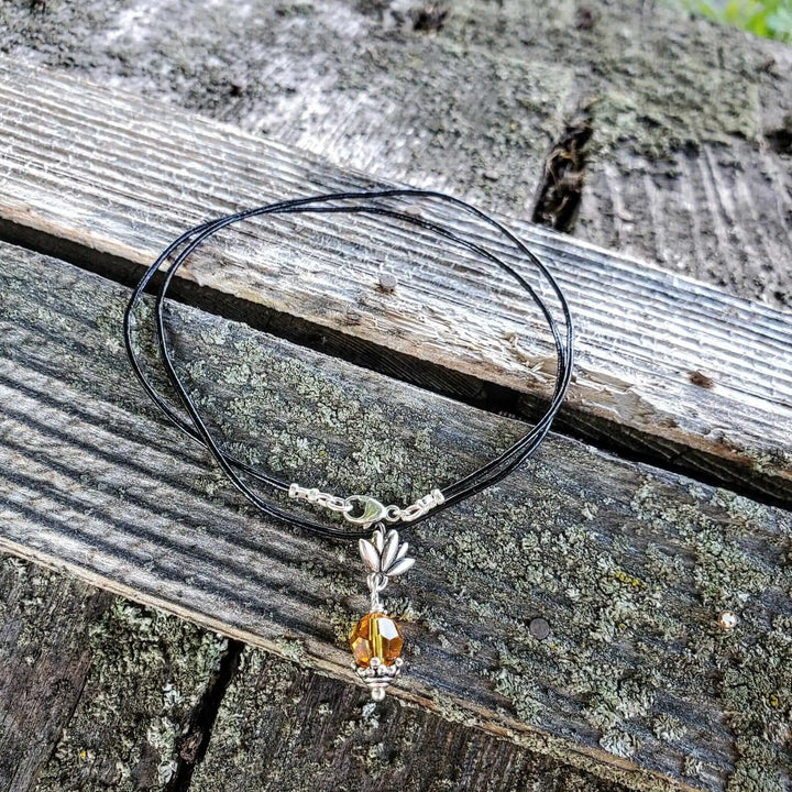 Handmade silver crystal pineapple leather necklace with yellow Austrian Swarovski crystal on a wooden background.