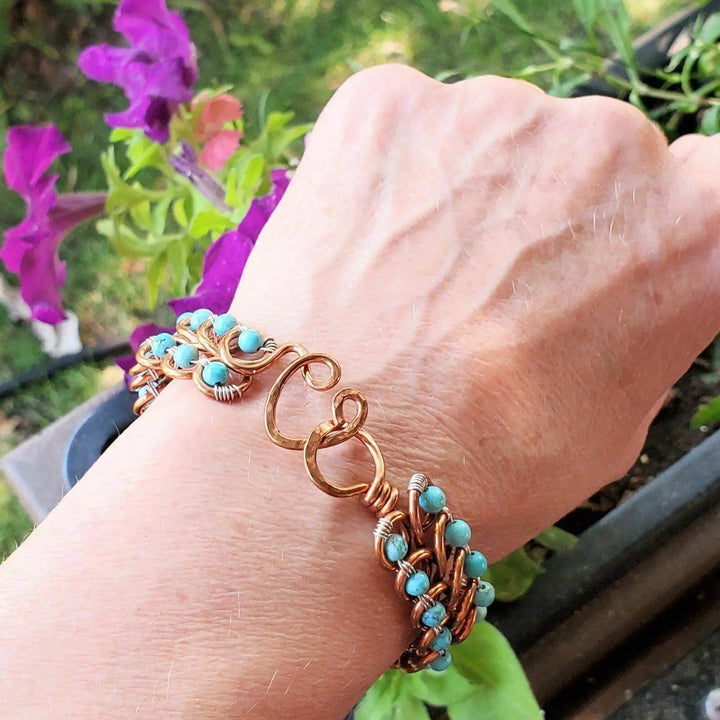 Wire Wrapped Turquoise Copper Infinity Heart Closure Bangle worn on wrist with turquoise beads and heart closure.