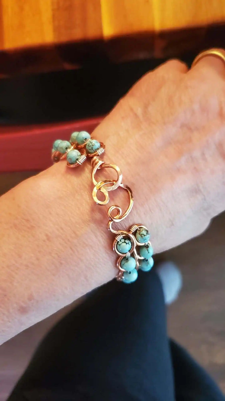 Wire Wrapped Turquoise Copper Infinity Heart Closure Bangle worn on wrist, showcasing turquoise crystals and heart closure.