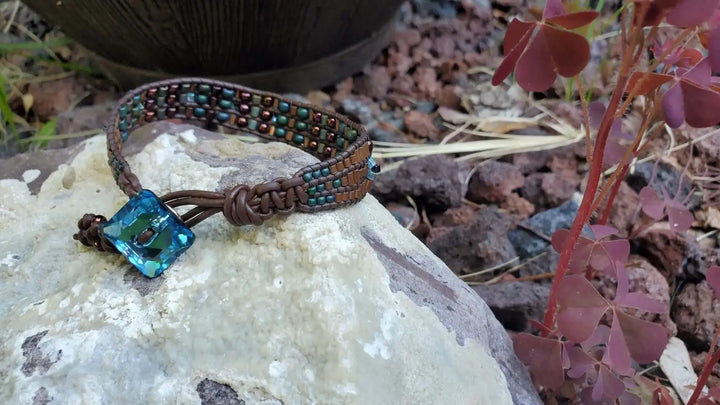 Intricate Bead Woven Swarovski Crystal Button Glam Bracelet displayed on a stone with colorful beads and a large aqua button.