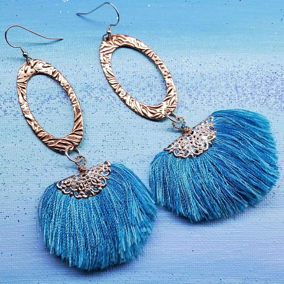 Long Copper Embossed Aqua Brushed Silk Fan Tassel Earrings on a blue background, featuring vibrant aqua silk tassels.