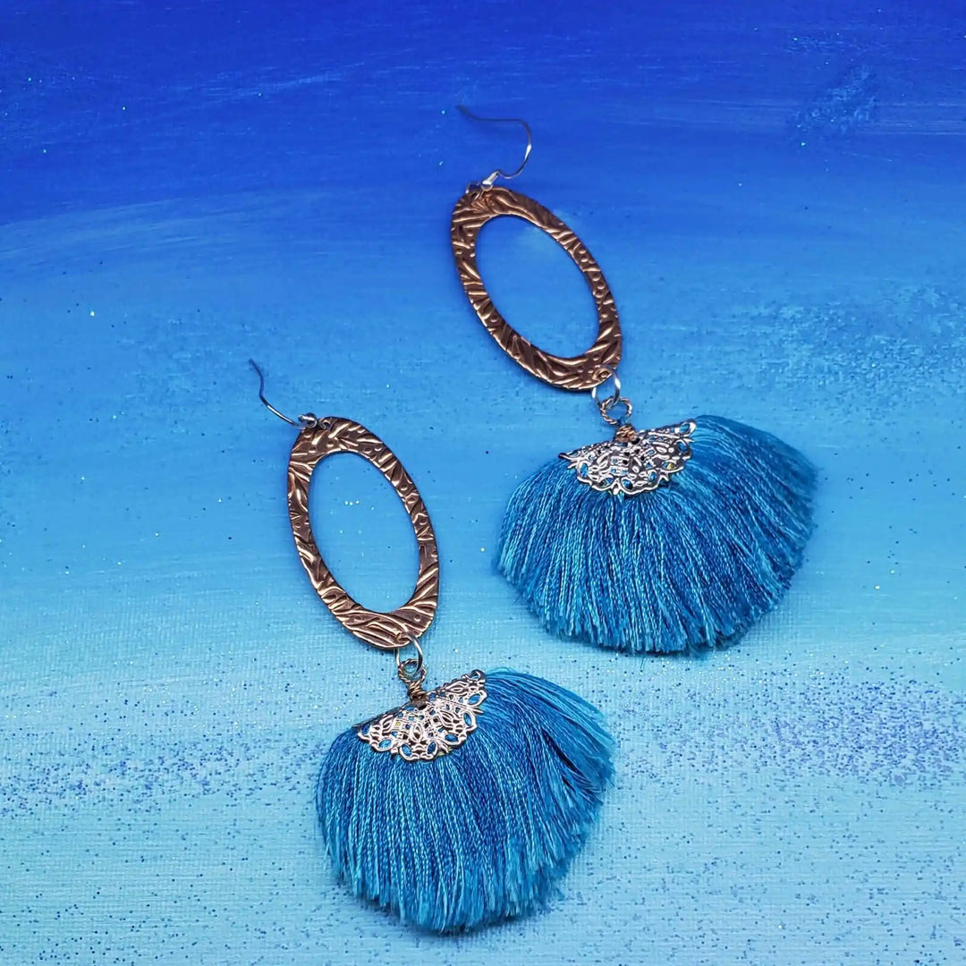 Long Copper Embossed Aqua Brushed Silk Fan Tassel Earrings on a blue background.