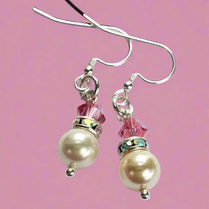 Various Color Swarovski Crystal Pearl Stack Earrings with pink and silver accents on a pink background.