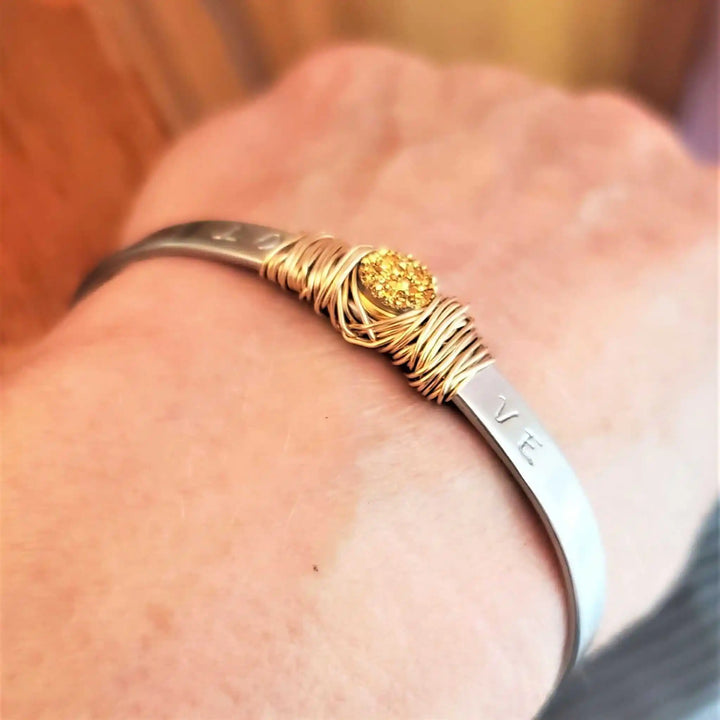 Stainless Steel LOVE Stamped Wire Wrapped Gold Druzy Cuff worn on wrist, showcasing handmade elegance.