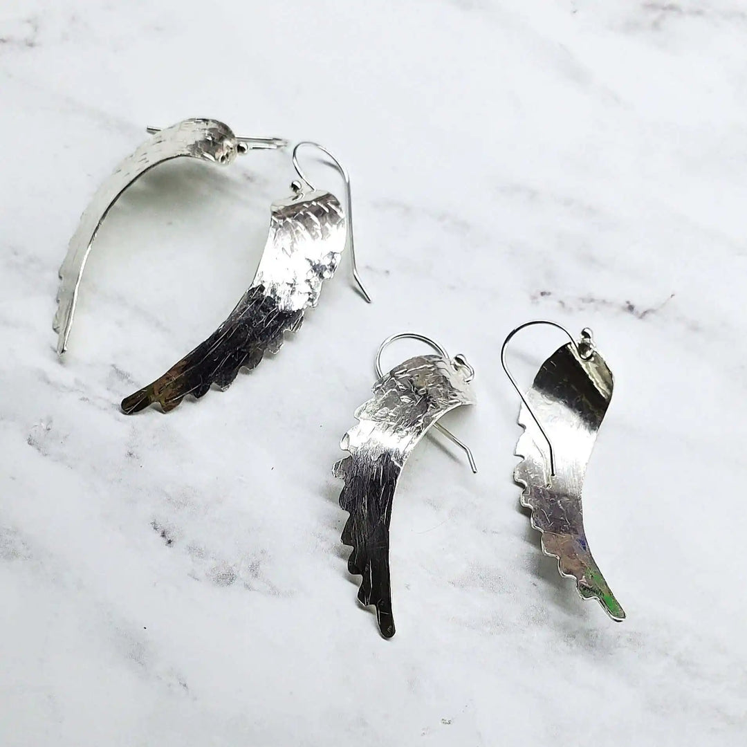 Silver Hammered Sculpted Angel Wing Earrings displayed on a marble background.