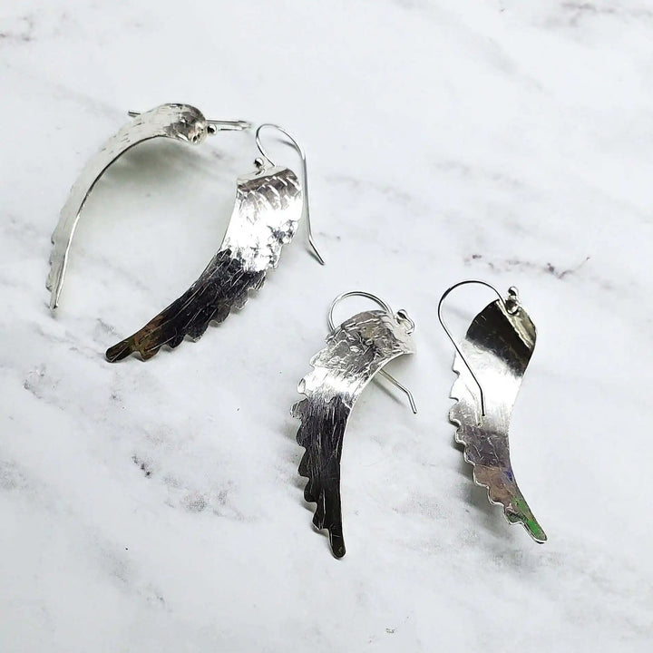 Silver Hammered Sculpted Angel Wing Earrings displayed on a marble background.