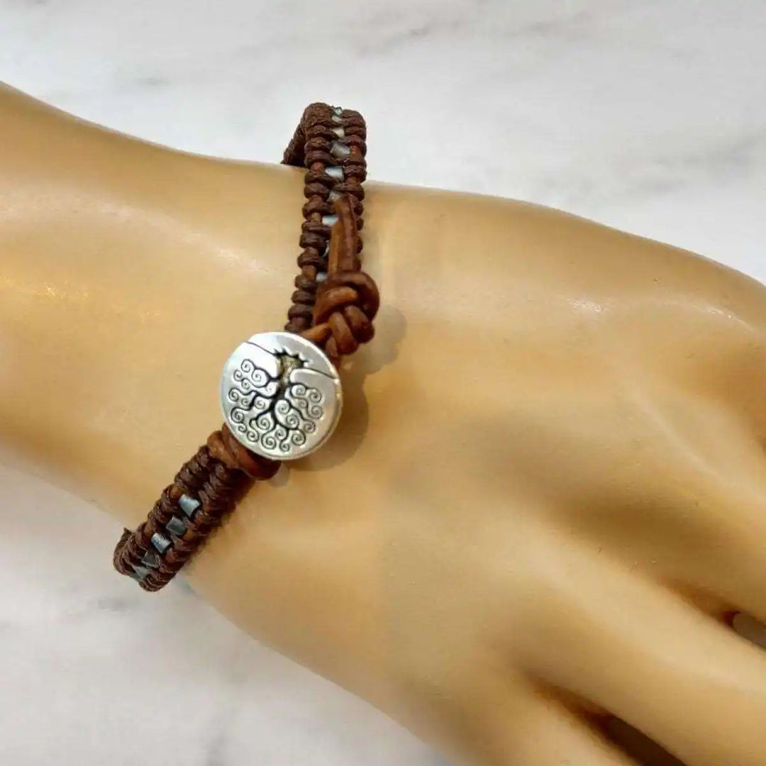Handmade Tree of Life leather wrap bracelet featuring brown and gray seed beads on a hand model.