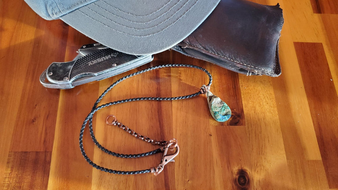Wire Wrapped Natural Cut Azurite Malachite Drop Necklace next to a wallet hat and pocket knife life style pictures