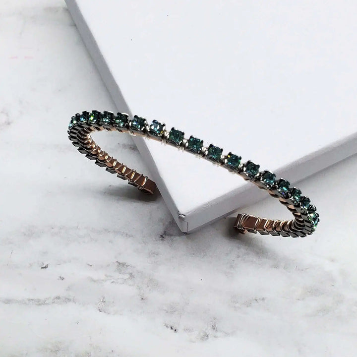 Wire Wrapped Turquoise Crystal Tennis Bangle Bracelet displayed on a marble surface, featuring aqua blue crystals on a copper bangle.